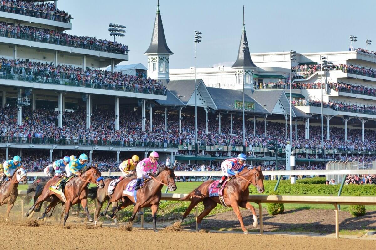 Horses race on a dirt track in front of a large crowd at Churchill Downs, with the iconic twin spires visible in the background—a classic scene from the Kentucky Derby. Discover more with our Kentucky Derby guide.