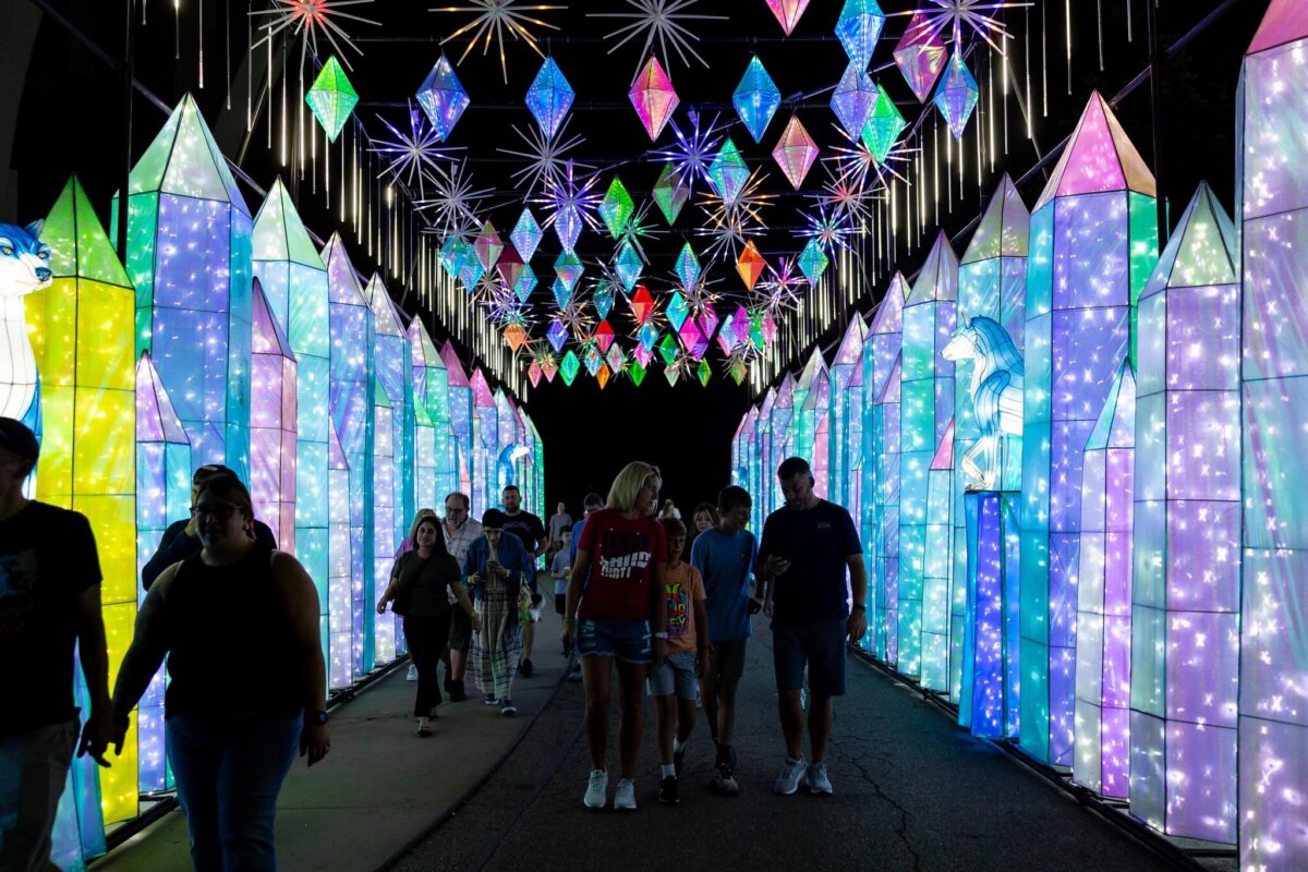 People walk through a brightly lit tunnel decorated with colorful illuminated geometric shapes and star-like lights at night, enjoying one of the dazzling Louisville happenings during May 2026.
