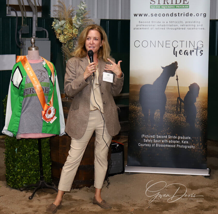Meet the Louisville Woman Giving Retired Racehorses a Second Chance - 4 A woman speaks into a microphone next to a banner for the Second Stride Equine Program and a mannequin displaying a ribbon and sash.