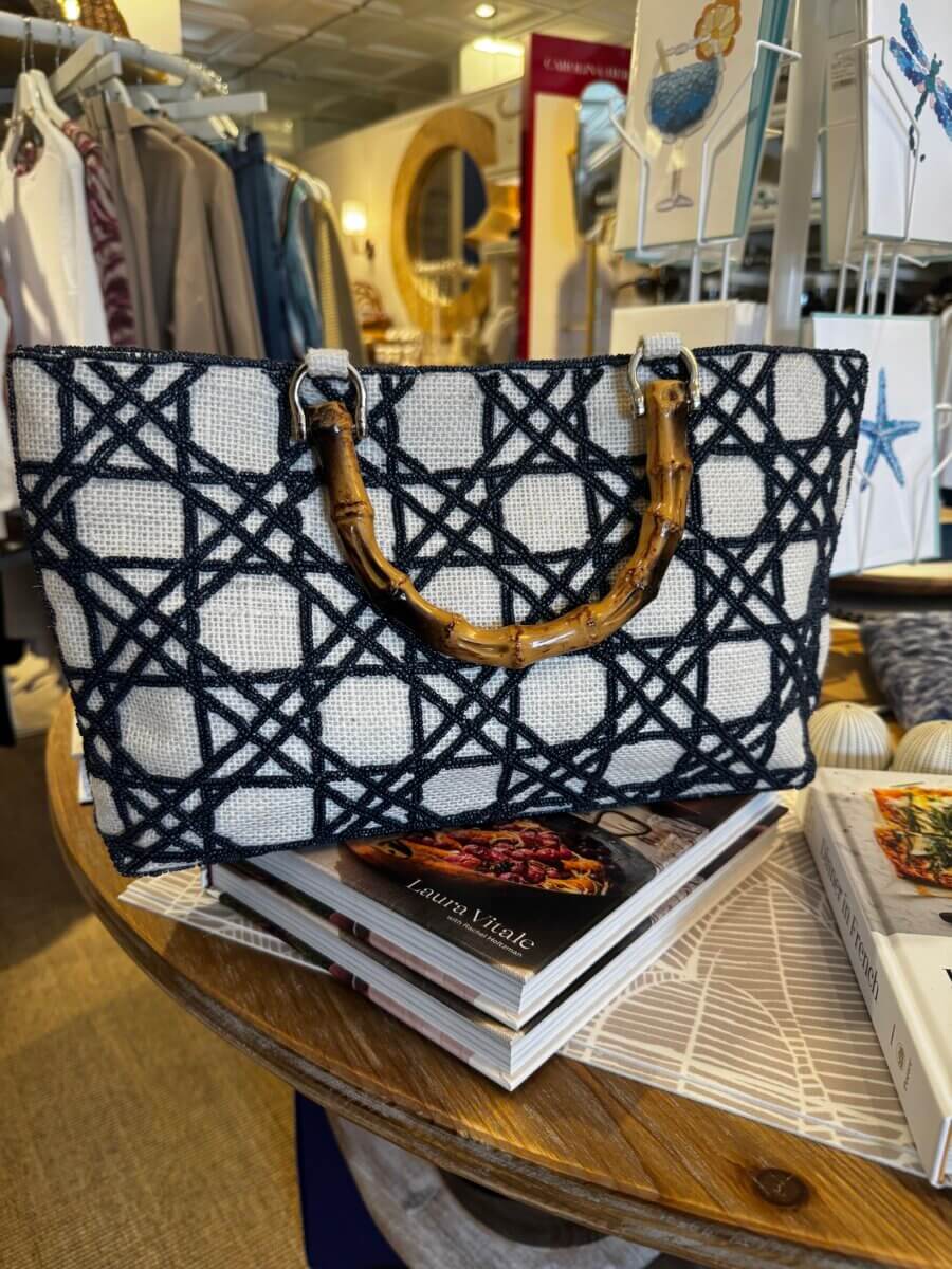 15 Louisville FINDS for May: Spring Fashion, Entertaining Essentials & More - 5 A woven handbag with bamboo handles sits on a stack of books on a round wooden table in a Louisville boutique, ready for your May FINDS.