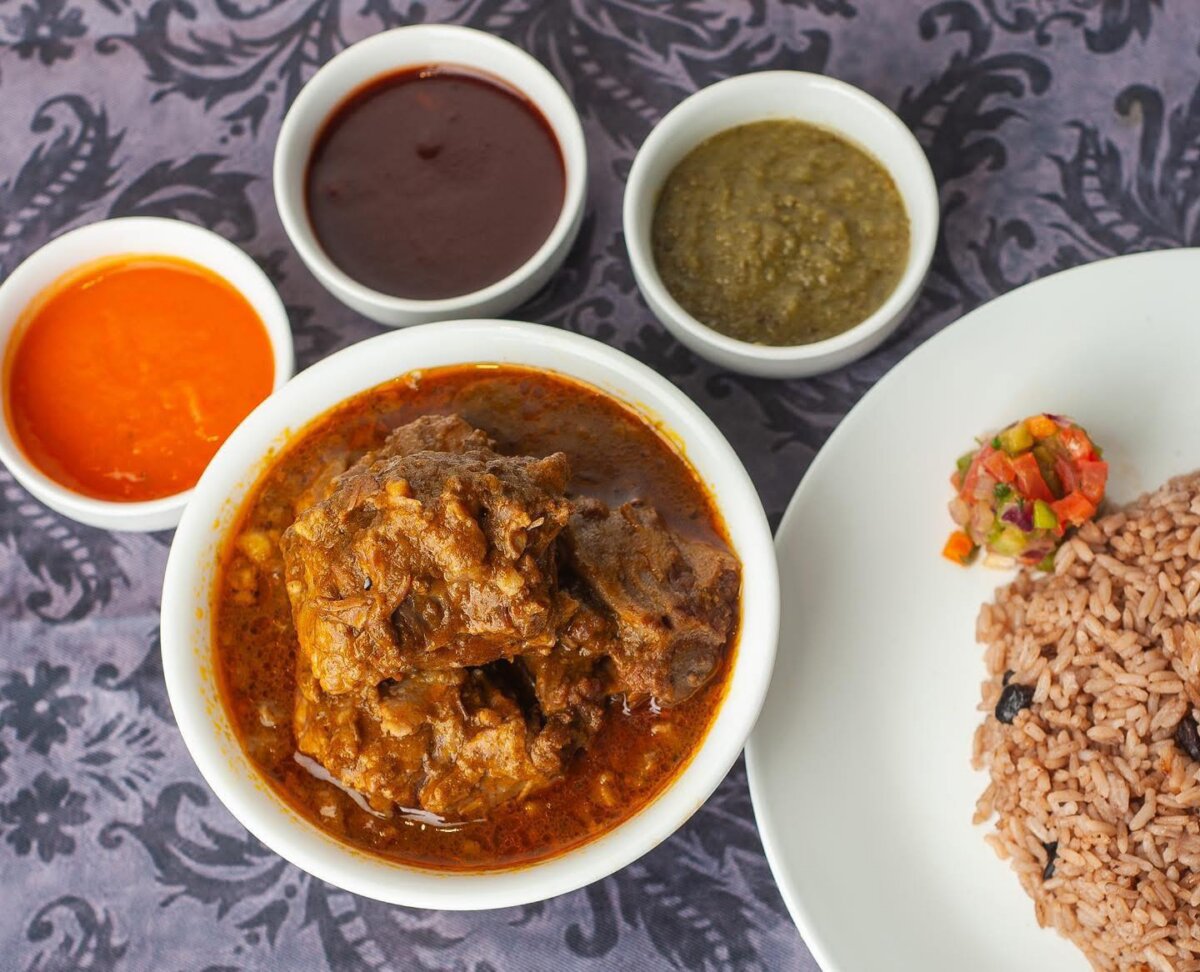 5 New Louisville Restaurants to Try This Month - 6 A bowl of stewed meat with three sauces in small bowls and a plate of rice with a small vegetable garnish on a patterned tablecloth.