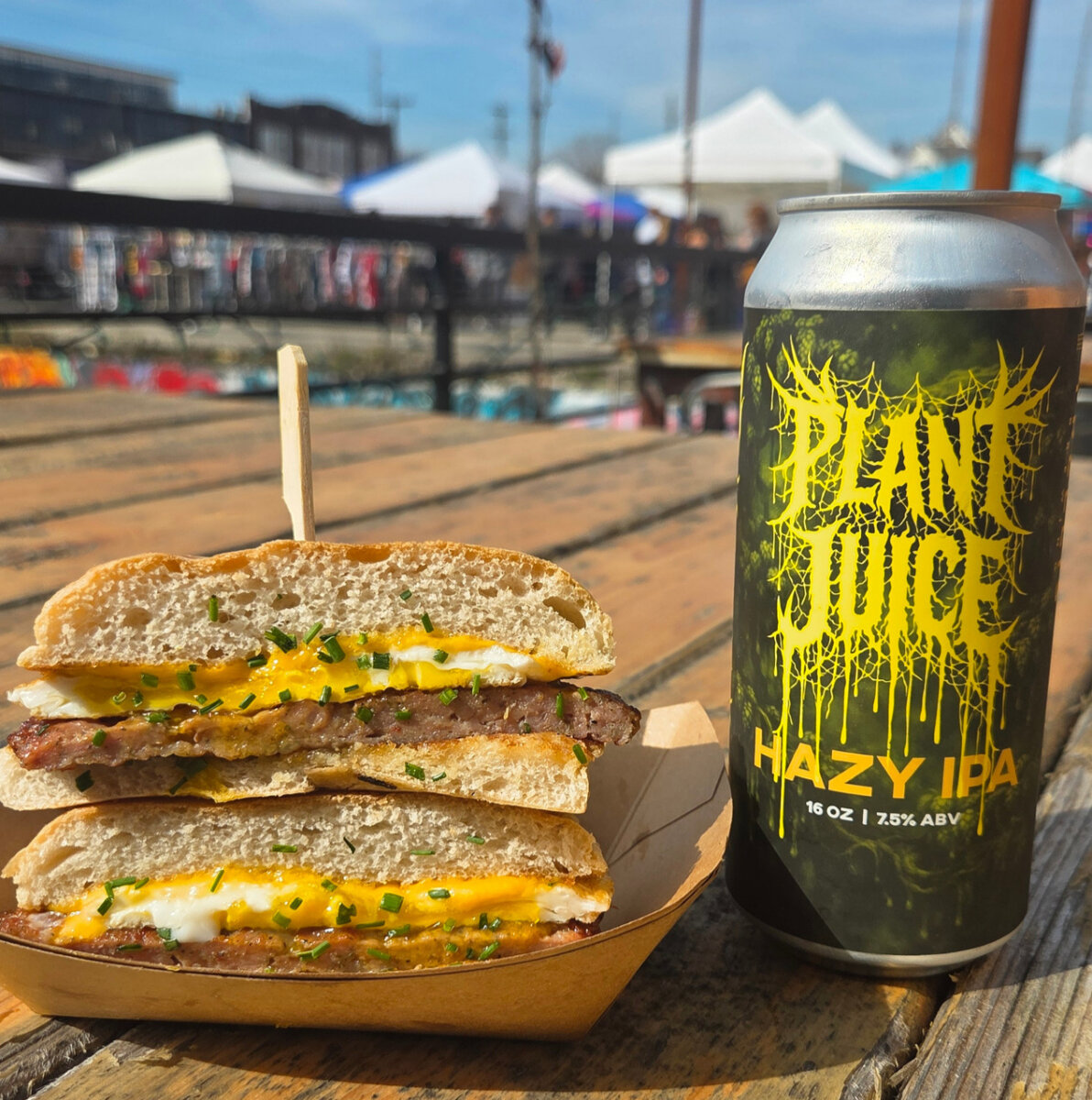 5 New Louisville Restaurants to Try This Month - 4 A stacked breakfast sandwich with egg, cheese, sausage, and chives sits next to a can of Plant Juice Hazy IPA on a wooden table at an outdoor market.