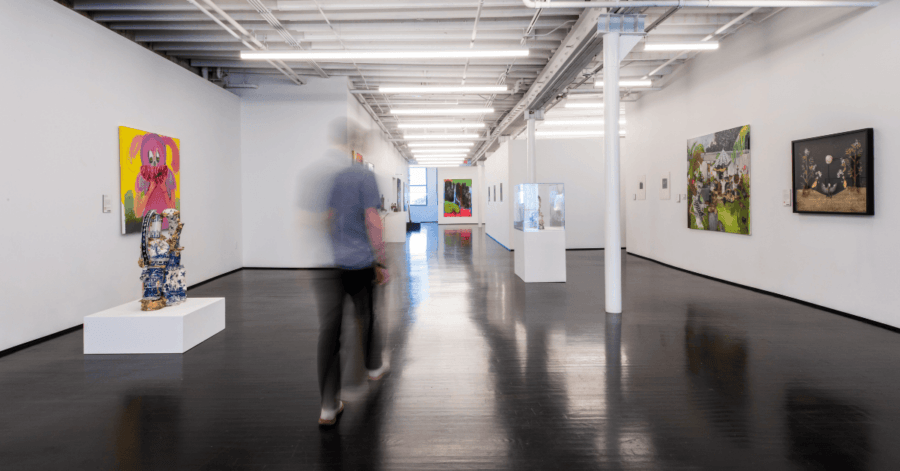 All-Ages Adventure: The Ultimate Trip to Louisville, KY - 11 A person enjoys an all-ages adventure, walking through a contemporary art gallery in Louisville with white walls, polished black floors, and diverse artworks displayed on the walls and pedestals.