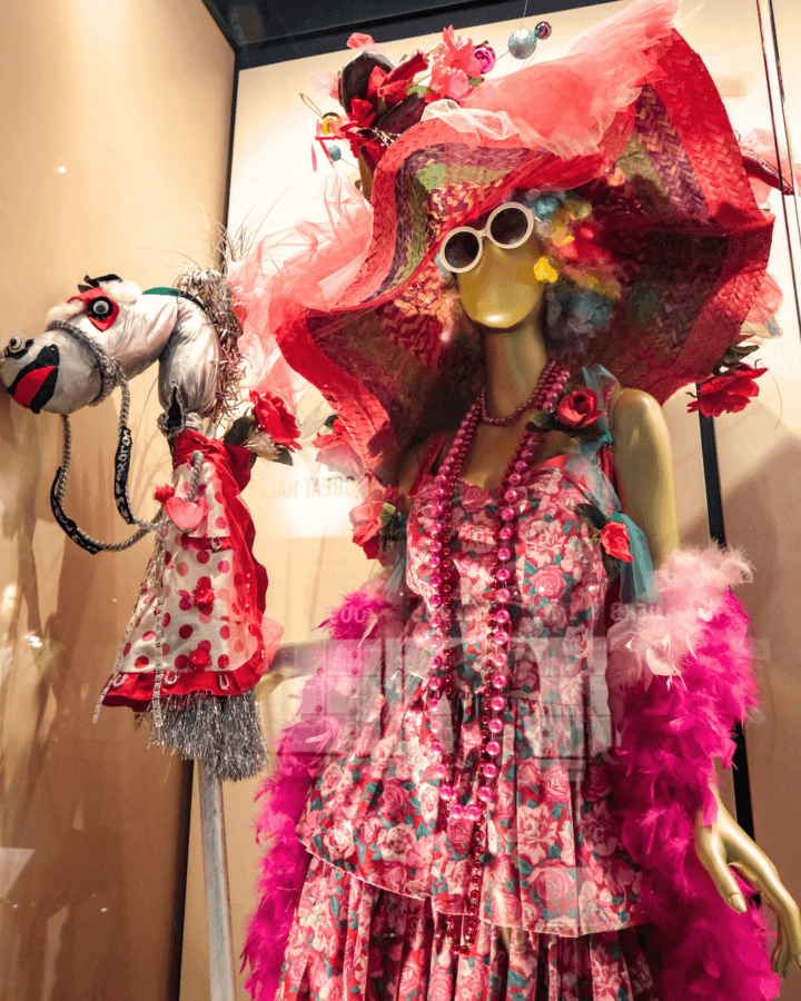 All-Ages Adventure: The Ultimate Trip to Louisville, KY - 3 A mannequin dressed in a colorful, layered floral dress, large hat, wig, sunglasses, pink beads, and boa stands next to a decorated hobby horse—a quirky highlight among things to do in Louisville—inside a display case.