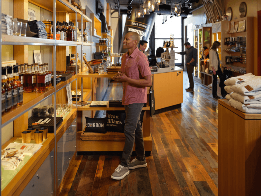 All-Ages Adventure: The Ultimate Trip to Louisville, KY - 16 A man browses shelves of spirits and merchandise in a well-lit liquor store with wood floors—one of the standout things to do in Louisville—while other customers shop in the background.