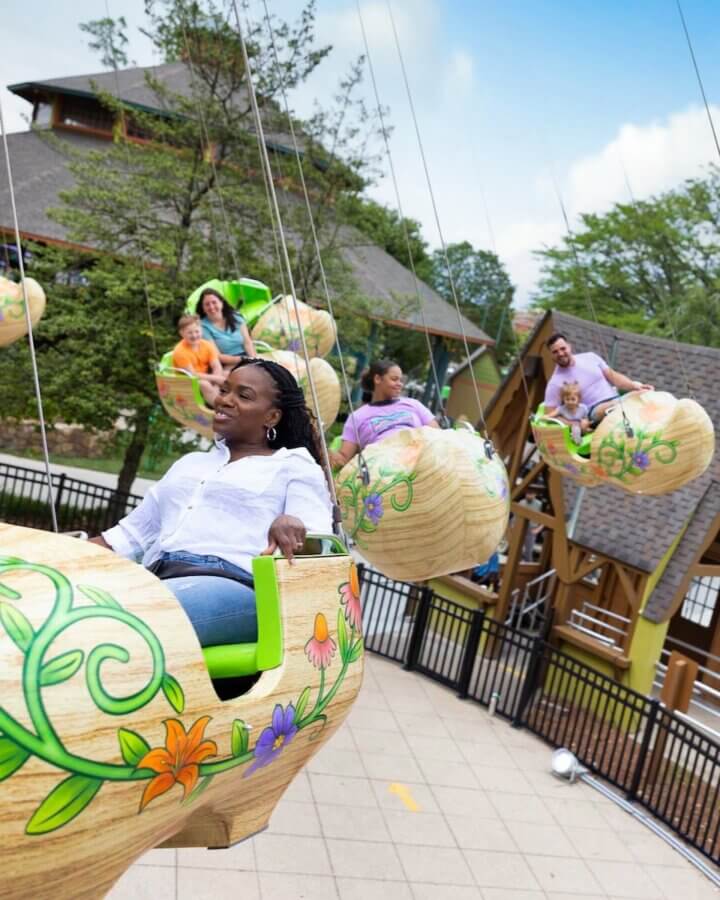 All-Ages Adventure: The Ultimate Trip to Louisville, KY - 6 Adults and children ride in decorative, flower-themed swing seats at an outdoor amusement park during the daytime—one of the delightful things to do in Louisville for families seeking fun.