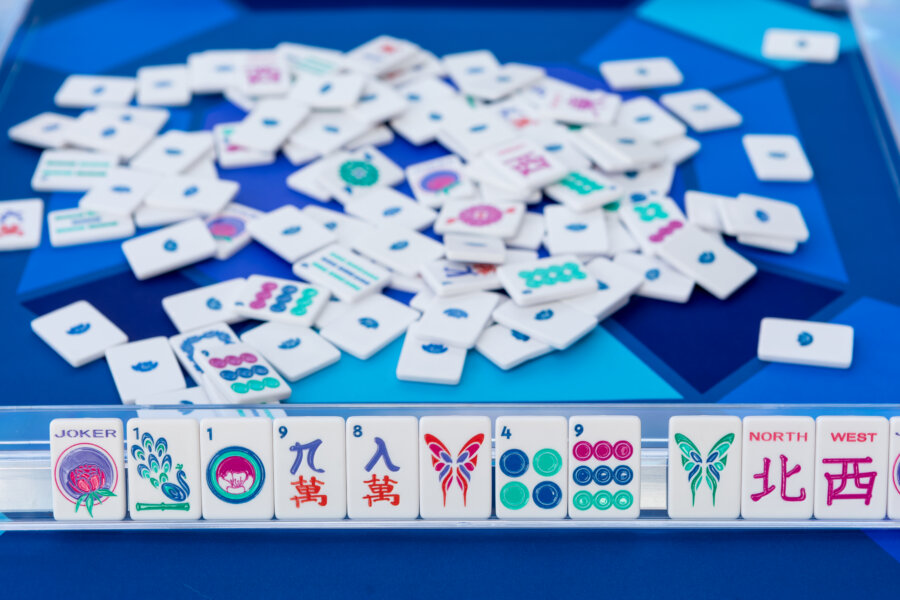 8 Mahjong Retreats Worth the Trip in 2026 - 6 A close-up of a Mahjong game with tiles arranged on a rack in the foreground and scattered tiles on a blue table in the background, evoking the relaxation often found at Mahjong retreats.
