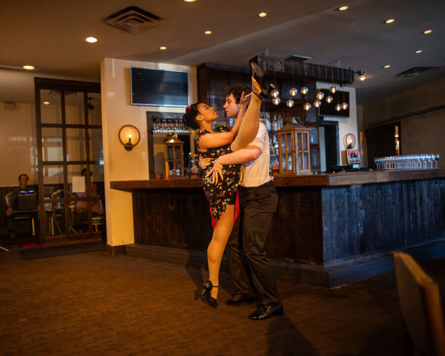 Ashley Hannah Davis Brings Memphis to Life Through Dance - 3 A pair of dancers perform a dramatic ballroom dance pose in a restaurant, with the woman lifting her leg high while the man supports her.