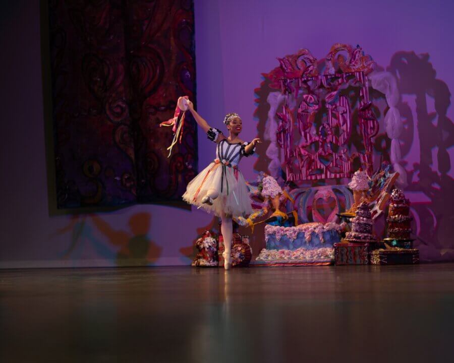 Ashley Hannah Davis Brings Memphis to Life Through Dance - 4 A performer in a colorful, patterned costume and tutu poses onstage with a prop, surrounded by ornate set decorations and dramatic lighting.