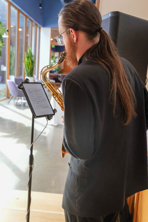 Meet the Creative Force Behind Soul88 & Civic Change in Memphis - 6 A person in a suit with long hair tied back plays a saxophone, reading sheet music from a stand in a modern indoor space with large windows.