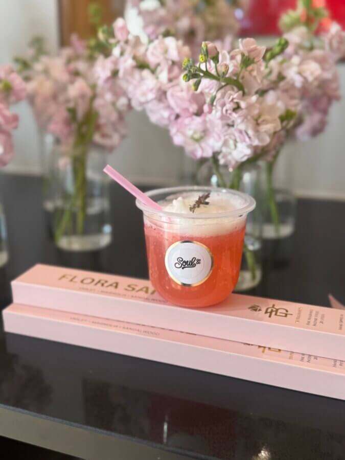 Meet the Creative Force Behind Soul88 & Civic Change in Memphis - 4 A plastic cup with a pink straw contains an orange drink with foam and a small garnish, placed on two pink books in front of vases of pink flowers, creating a vibrant scene.