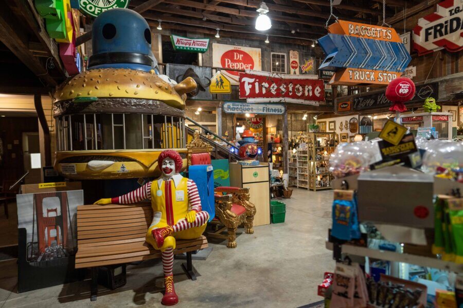 Why Hattiesburg Might Be Mississippi’s Biggest Surprise - 5 A colorful indoor display in Hattiesburg, Mississippi features a large hamburger structure, a Ronald McDonald statue on a bench, vintage signs, and various memorabilia—offering visitors the biggest surprise in this cluttered setting.