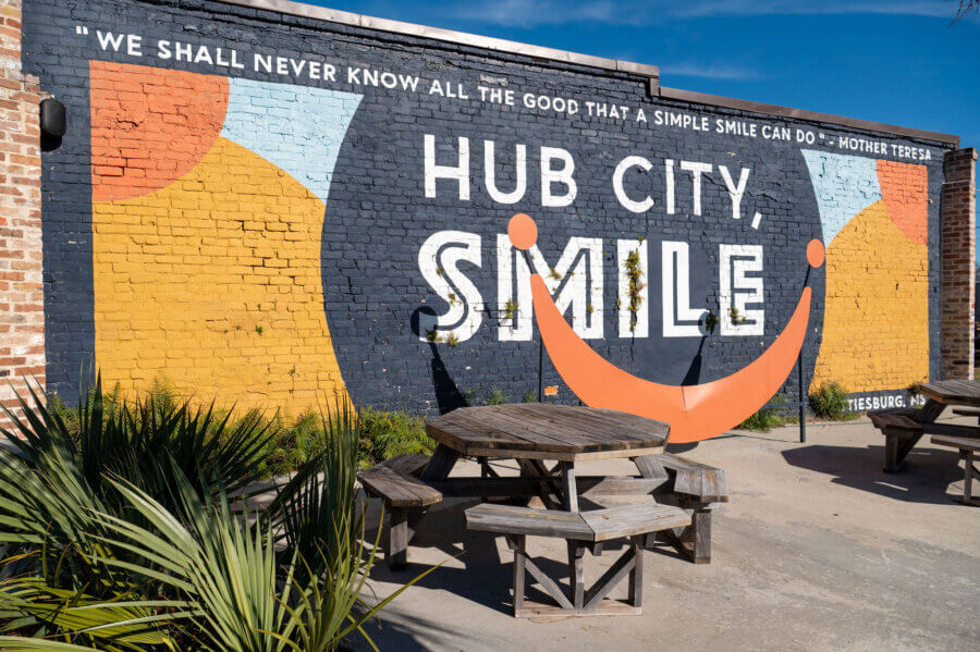 Why Hattiesburg Might Be Mississippi’s Biggest Surprise - 7 A mural with the words "HUB CITY, SMILE" and a large orange smile adds charm to an outdoor seating area in Hattiesburg, Mississippi.