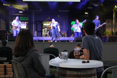 A band performs live music on stage at an outdoor venue with patios, while people sit at tables in the audience, some holding drinks—a classic scene at Memphis restaurants.