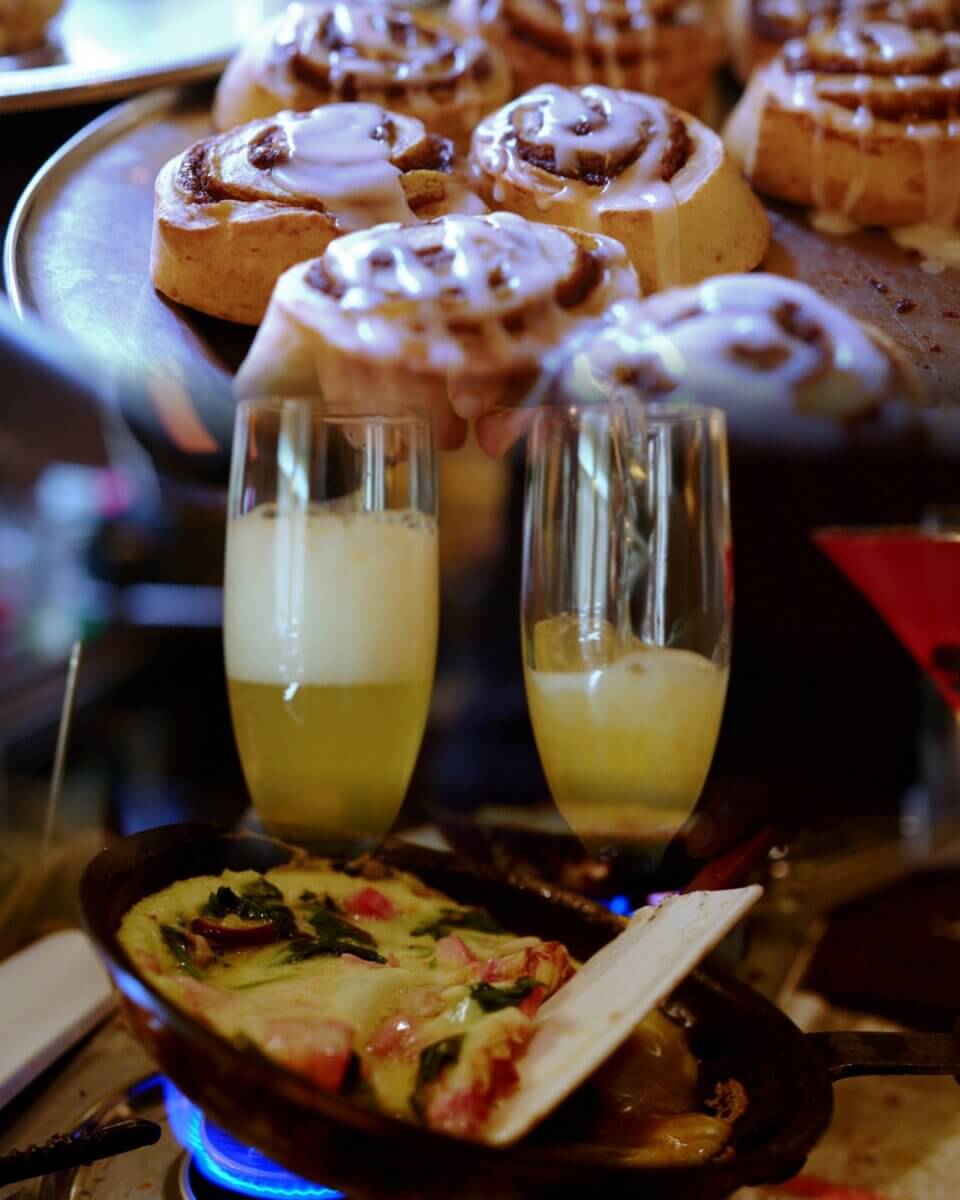 Where to Get Mother's Day Brunch in Memphis - 10 Enjoy a delightful Mother's Day Brunch in Memphis with cinnamon rolls topped with icing, two glasses of sparkling drink, and a skillet omelet filled with fresh vegetables and seafood simmering on the stovetop.