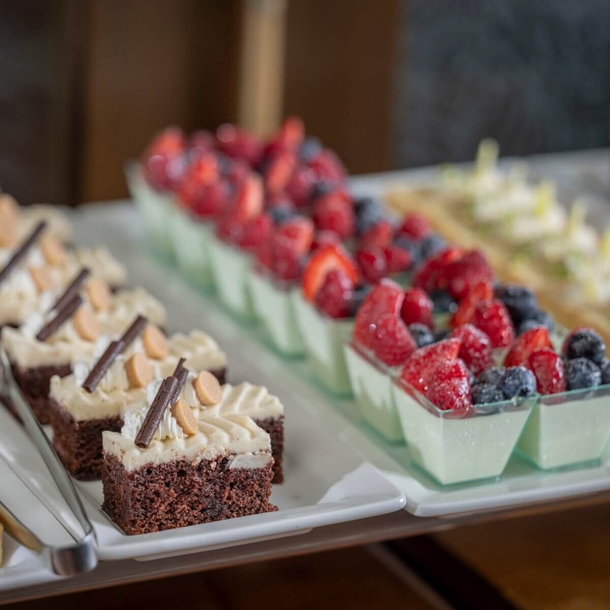 Where to Get Mother's Day Brunch in Memphis - 15 Assorted desserts on a tray, including chocolate cake squares with cream and chocolate garnish, and glass cups with mousse topped with strawberries and blueberries—perfect for a Mother's Day Brunch in Memphis.