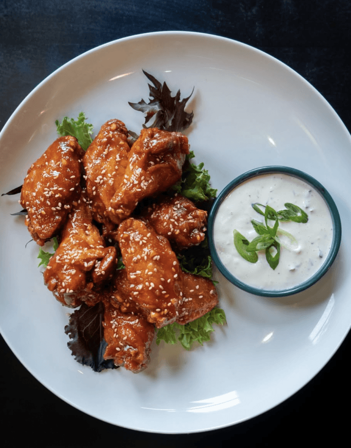 5 New Memphis Restaurants to Try This Month (+ What's Coming Soon!) - 6 A plate of sauced chicken wings garnished with sesame seeds and greens, served with a side of ranch dip topped with sliced green onions.