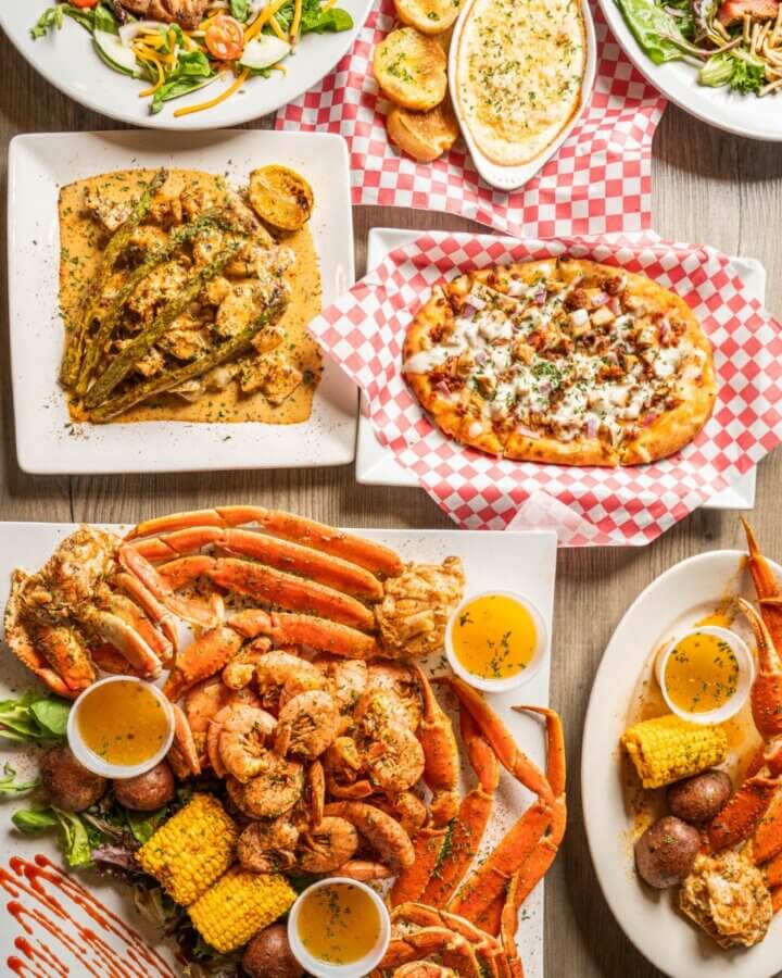 Your Guide to Coastal Mississippi’s Seafood Scene - 10 A table displays assorted Coastal MS Cuisine: crab legs, shrimp, corn, potatoes, salad, flatbread pizza, and a baked cheese appetizer—perfect for those eager to explore top Seafood Spots when they Visit MS.