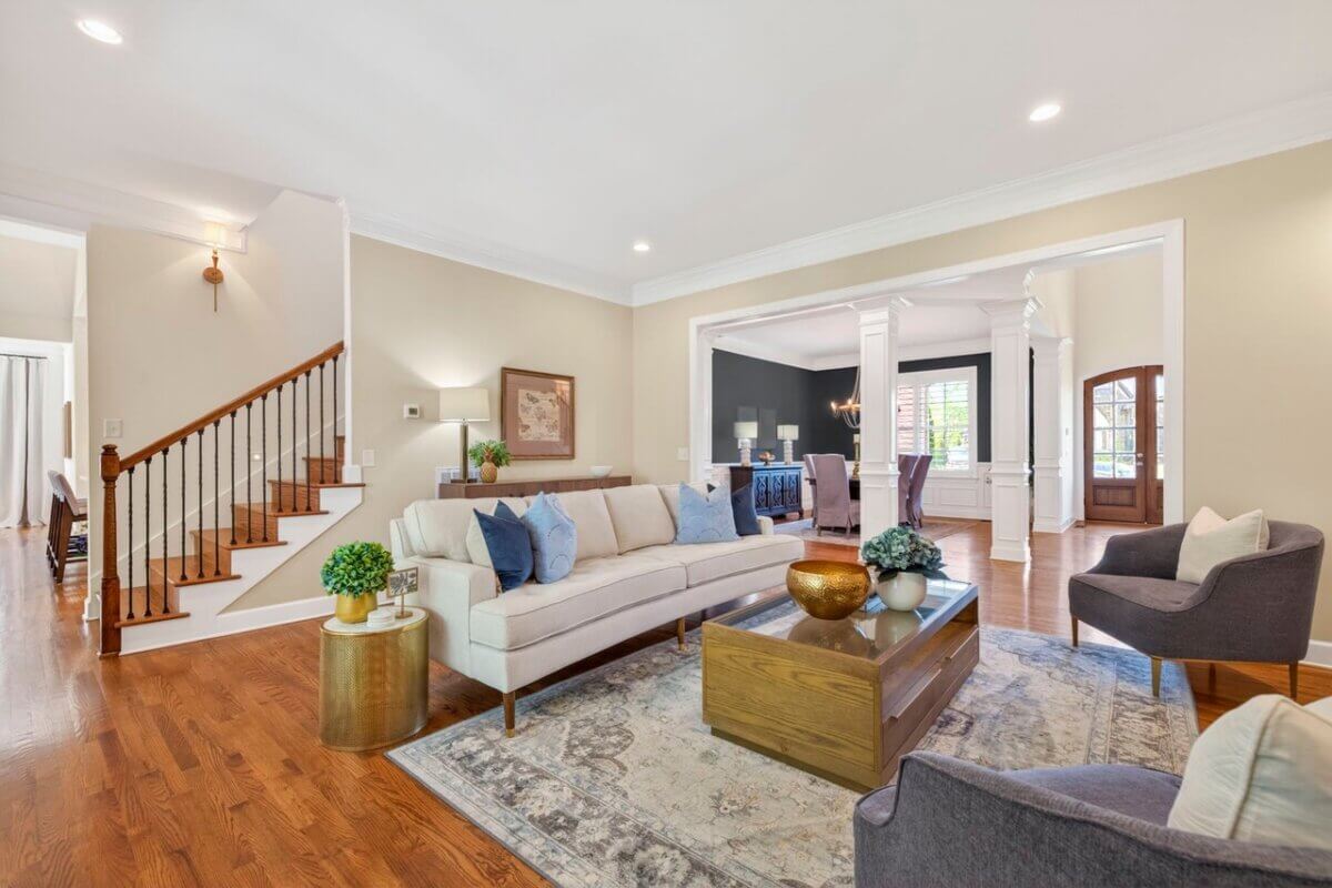 Just Listed! A Thoughtfully Designed Franklin Home That Delivers on Every Level - 5 A spacious living room at 2708 Eglington Terrace features a beige sofa, two gray chairs, a wooden coffee table, and a staircase; an adjoining room is visible through the wide entryway.