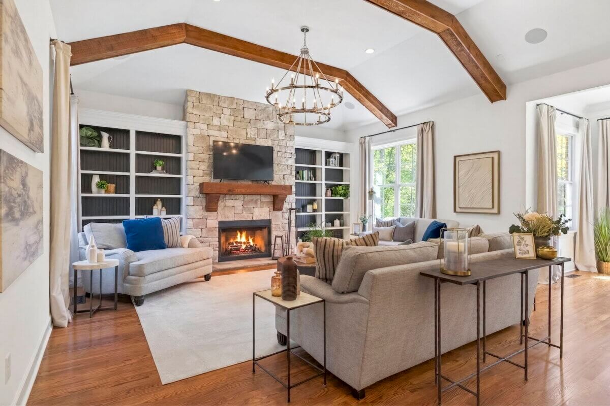 Just Listed! A Thoughtfully Designed Franklin Home That Delivers on Every Level - 6 A living room features exposed wood beams, a stone fireplace, built-in shelves, sofas, a chandelier, and large windows flooding the space with natural light.