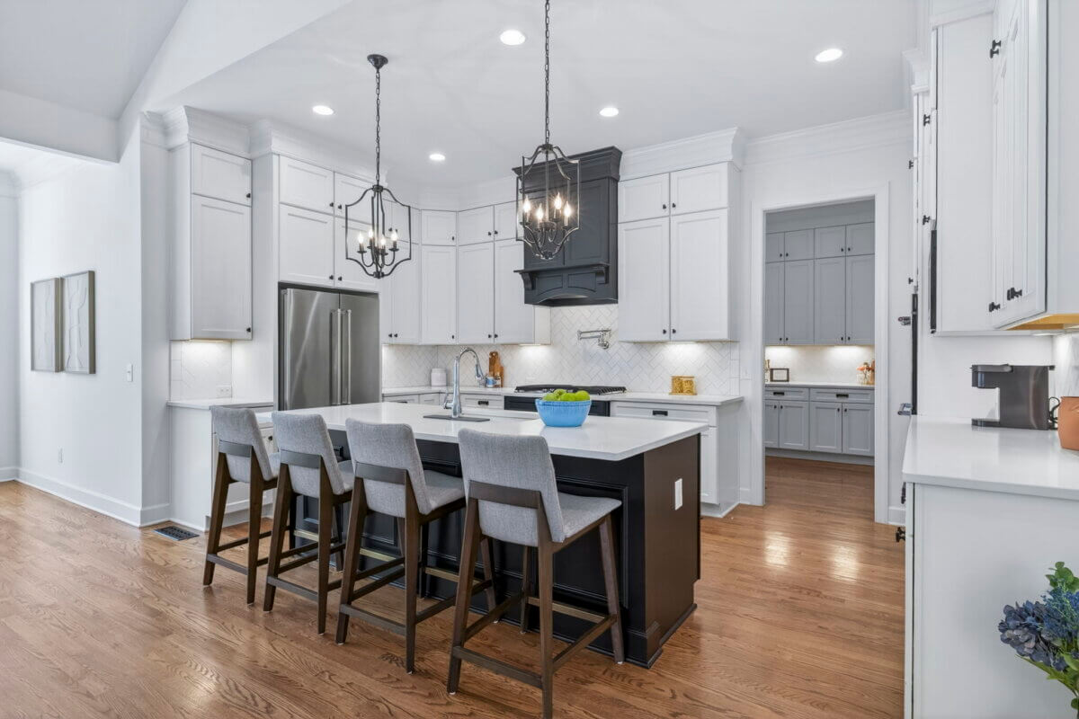 Just Listed! A Thoughtfully Designed Franklin Home That Delivers on Every Level - 8 Modern kitchen with white cabinets, black island, stainless steel appliances, four gray bar stools, pendant lights, and wood flooring. A bowl of green apples sits on the island.