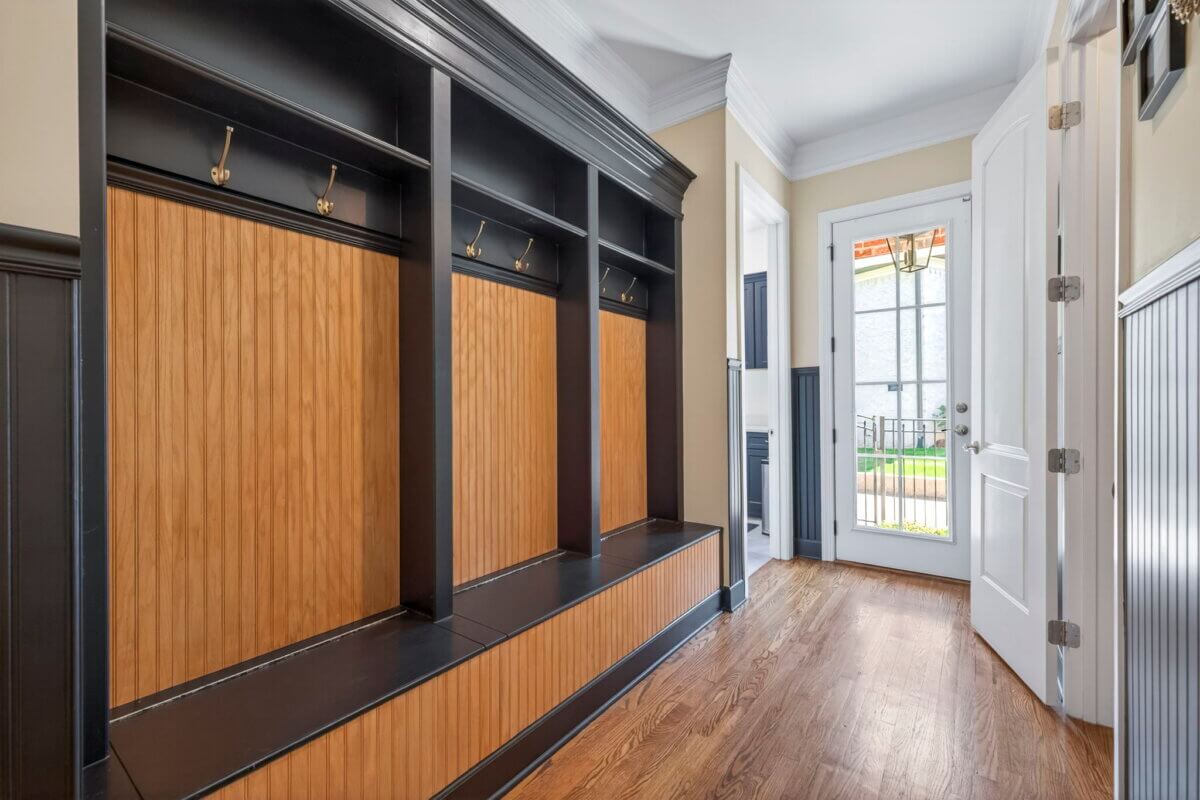 Just Listed! A Thoughtfully Designed Franklin Home That Delivers on Every Level - 15 A hallway with built-in wooden cubbies, black trim, hooks, and a bench leads to a glass door opening to the outdoors.