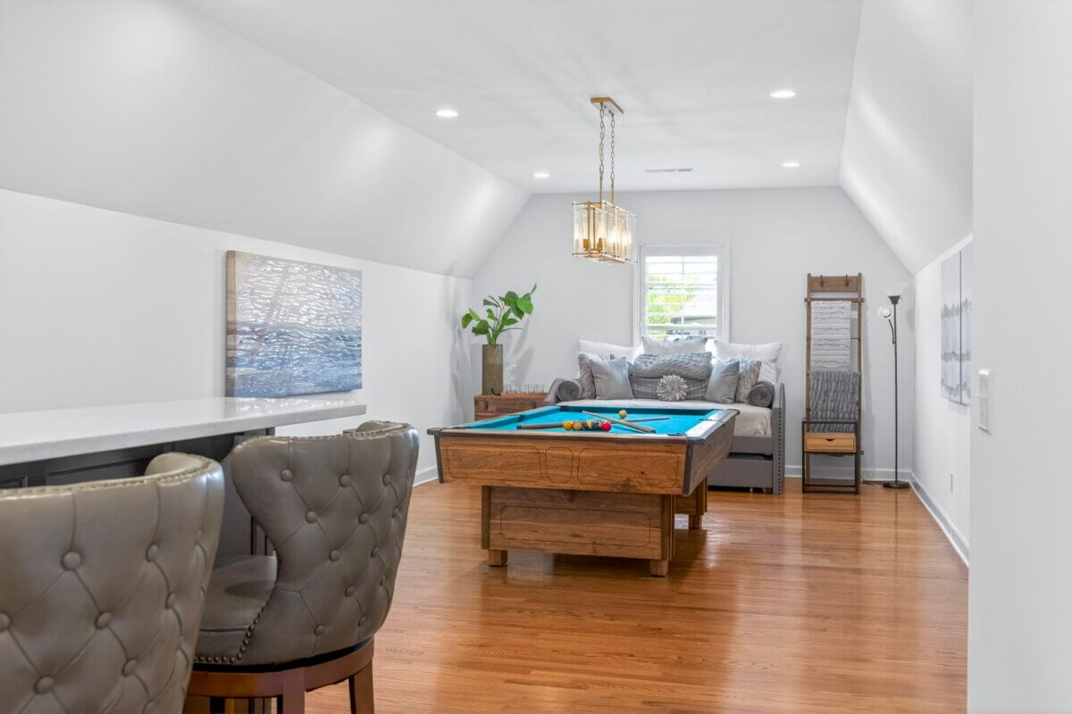 Just Listed! A Thoughtfully Designed Franklin Home That Delivers on Every Level - 14 A bright game room features a pool table, tufted chairs at a counter, a cozy couch with pillows, artwork on the walls, and a large window flooding the space with natural light.