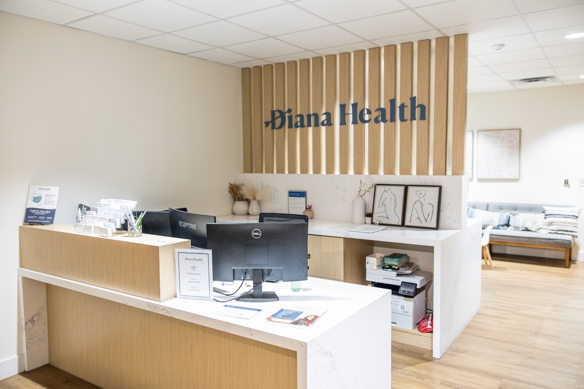 Inside the 'Whole Health' Approach Changing Women’s OB/GYN Care - 2 Reception area of Diana Health clinic, featuring a front desk with computers, informational brochures on our whole health approach, and modern minimalist decor.