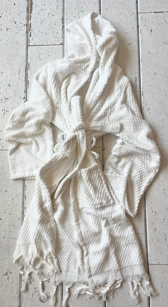 20 Spring FINDS for Mother’s Day & Beyond: Style, Beauty & Home Must-Haves - 8 A white, textured bathrobe with a hood, waist tie, and fringed edges is laid out on a white wooden floor, ready for relaxation after a long day at the Nashville FINDS Draft in May 2026.