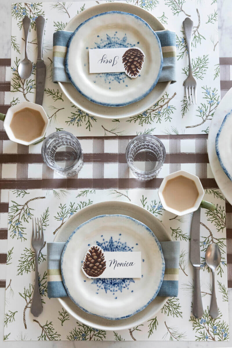 Nashville Steals, Deals & Announcements: May 2026 - 2 Two place settings with blue-and-white plates, striped napkins, cutlery, glasses, cups, and pinecone name cards rest on patterned placemats—perfect for sharing Nashville Steals on your next gathering.