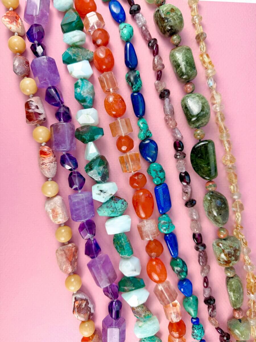 Nashville Steals, Deals & Announcements: May 2026 - 5 Several colorful beaded necklaces made from various stones and crystals are arranged side by side on a pink surface, ready to brighten your day with these Nashville Deals.