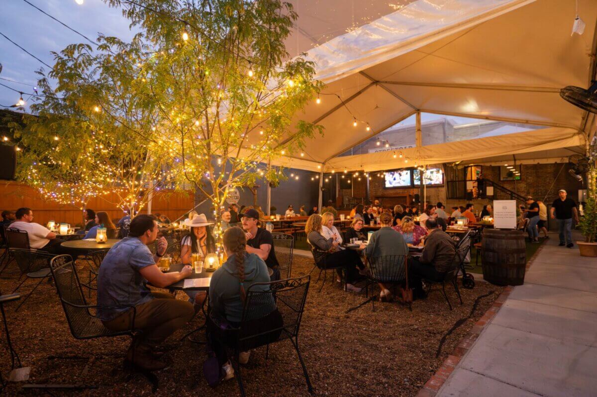 Nashville Steals, Deals & Announcements: May 2026 - 8 Outdoor restaurant patio with string lights and trees, people sitting at tables eating and talking under a large tent canopy in the evening—don’t miss the latest Nashville Deals for an unforgettable night out.