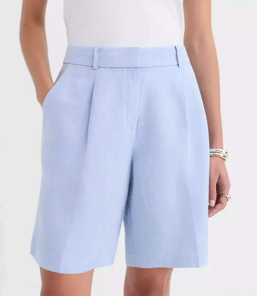 A man wearing light blue tailored knee-length shorts and a white top, with his hands in his pockets and a silver bracelet on one wrist.