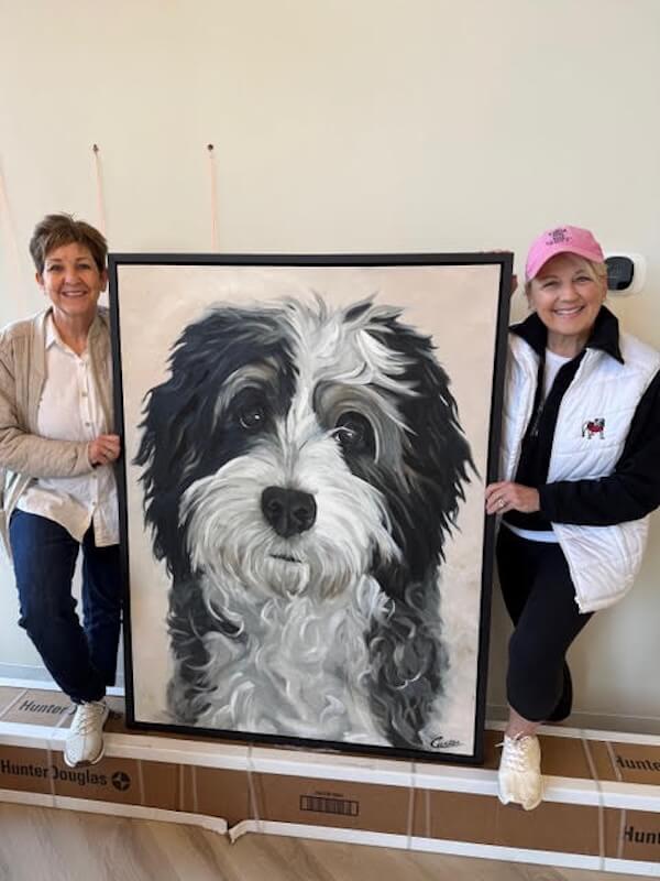Not Your Average Vet: A Beautifully Designed Georgia Clinic Inspired by One Dog's Story - 7 Two women pose indoors with a large painted portrait of a black-and-white dog.