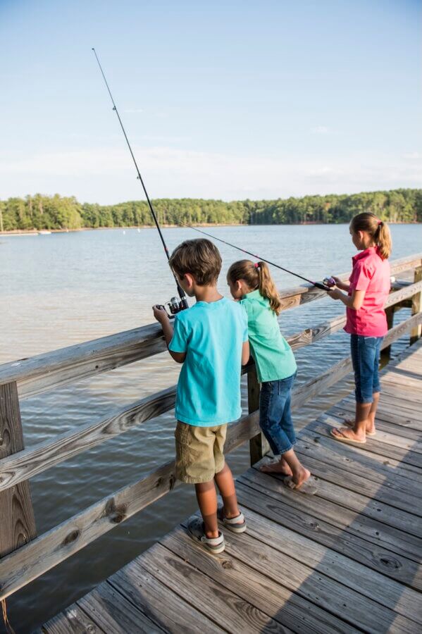 The Top Outdoor Adventures in South Carolina - 9 Three children enjoy outdoor adventures in South Carolina, fishing from a wooden dock by a lake, holding fishing rods and gazing at the water.
