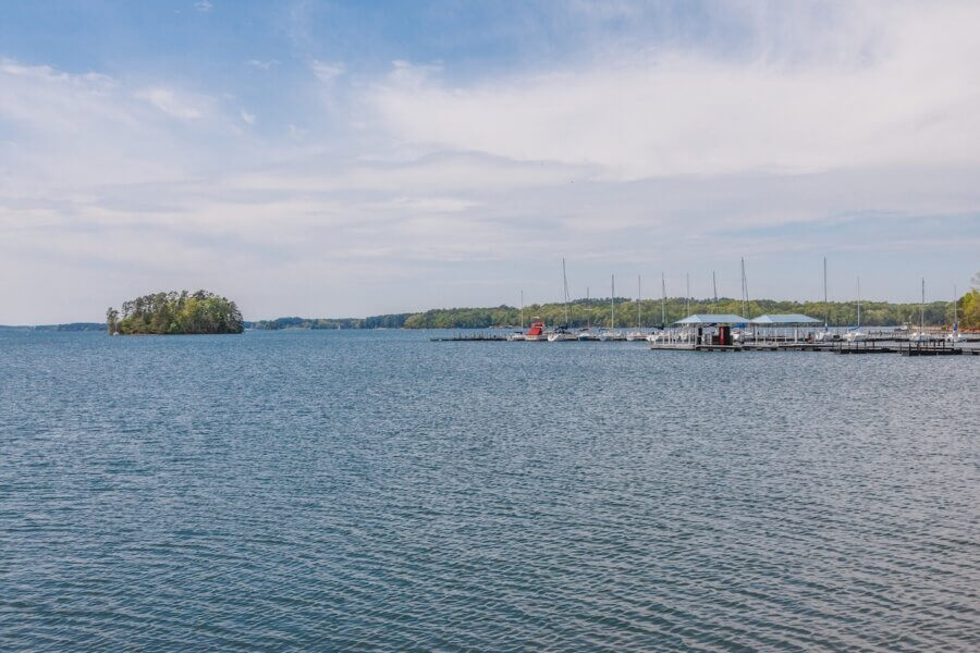 The Top Outdoor Adventures in South Carolina - 5 A calm lake in South Carolina with a small wooded island on the left, a marina with sailboats on the right, and a partly cloudy sky overheadβperfect for outdoor adventures.