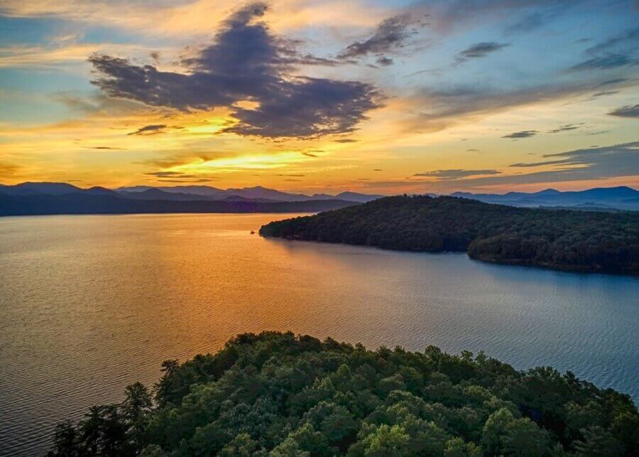 The Top Outdoor Adventures in South Carolina - 4 Aerial view of a lake at sunset with tree-covered hills in the foreground and distant mountains under a partly cloudy skyβperfect for Outdoor Adventures in South Carolina.