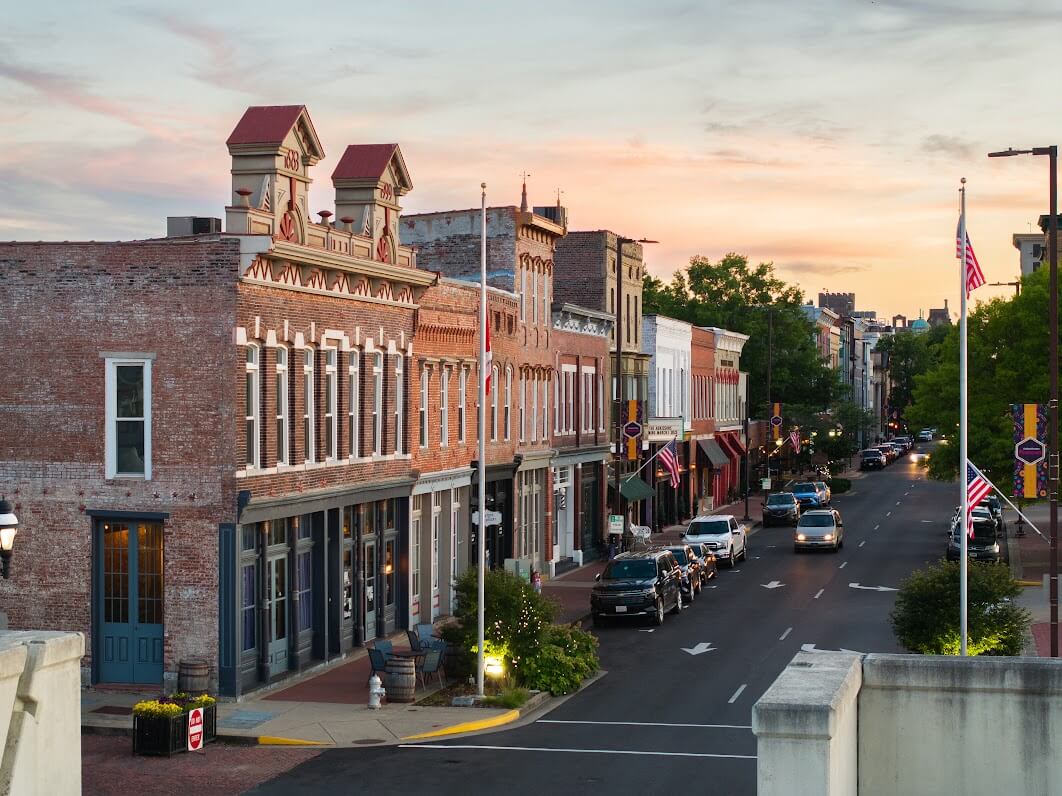 Need a Change of Scenery? Try These Summer Weekend Trips From Nashville - 6 A view of a historic downtown street in Nashville with brick buildings, parked cars, American flags, and trees at sunset—perfect for inspiring summer weekend trips or relaxing weekend getaways.