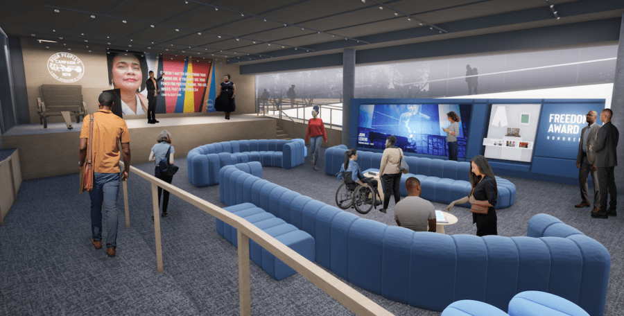 Living History: 7 Tennessee Towns Where the Past Comes Alive - 15 People interact in a modern, open room with blue seating, a stage, digital displays, and large photos of historic towns on the walls; one person uses a wheelchair.