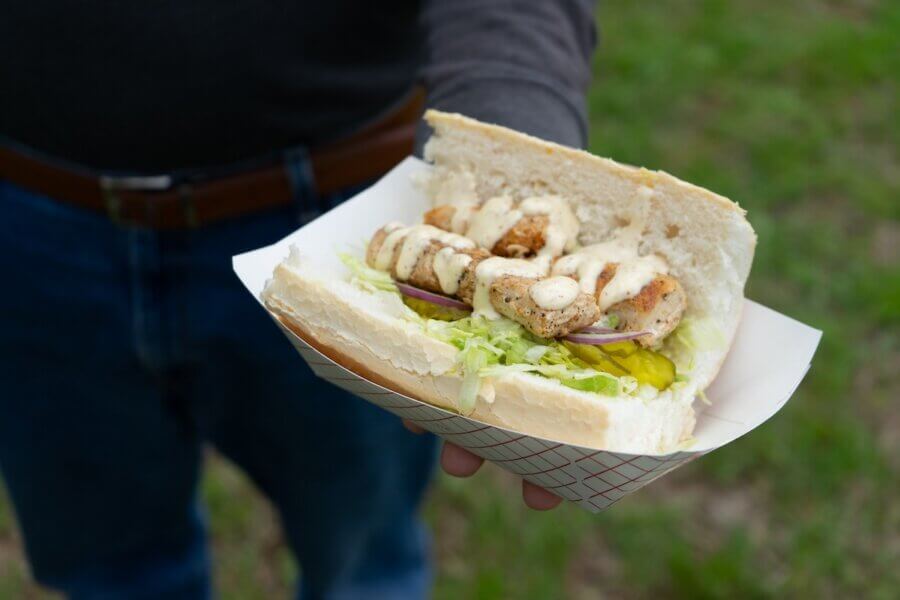 Living History: 7 Tennessee Towns Where the Past Comes Alive - 13 A person holding a paper tray with a sandwich containing grilled chicken, lettuce, pickles, onion, and sauce in a sliced white roll—perfect for exploring historic towns.