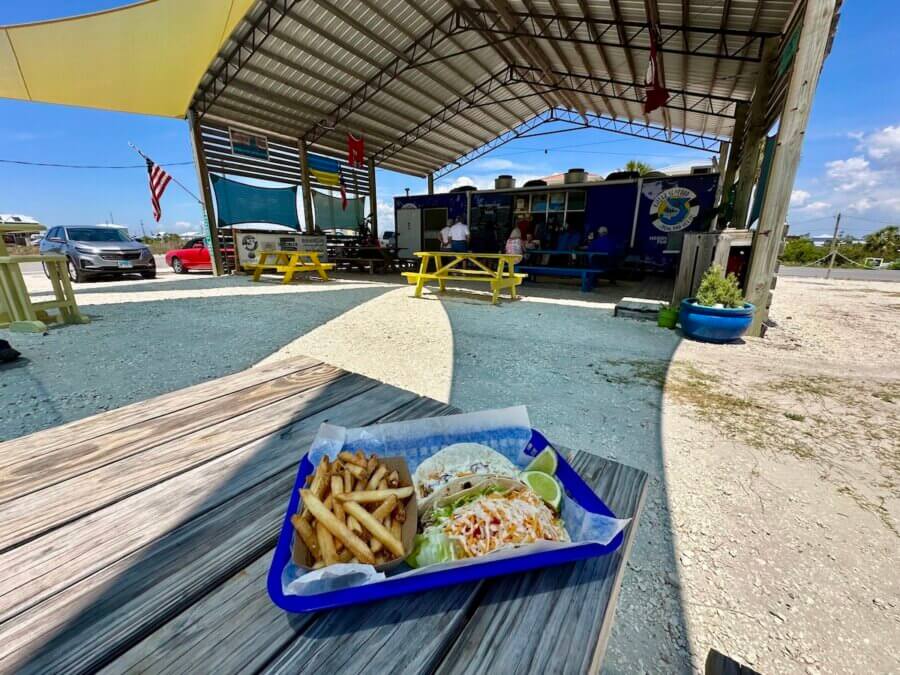 6 Southern Waterfront Weekend Escapes - 9 A tray with fries, cole slaw, and a taco sits on a wooden table outside a casual food stand along the Southern Waterfront, with picnic tables under a canopy.