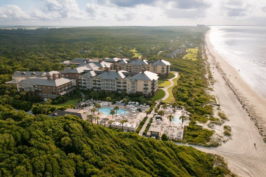 6 Southern Waterfront Weekend Escapes - 4 Aerial view of a large beachfront resort from Southern Waterfront, featuring multiple pools amid lush greenery, next to a sandy beach and ocean under a partly cloudy sky.