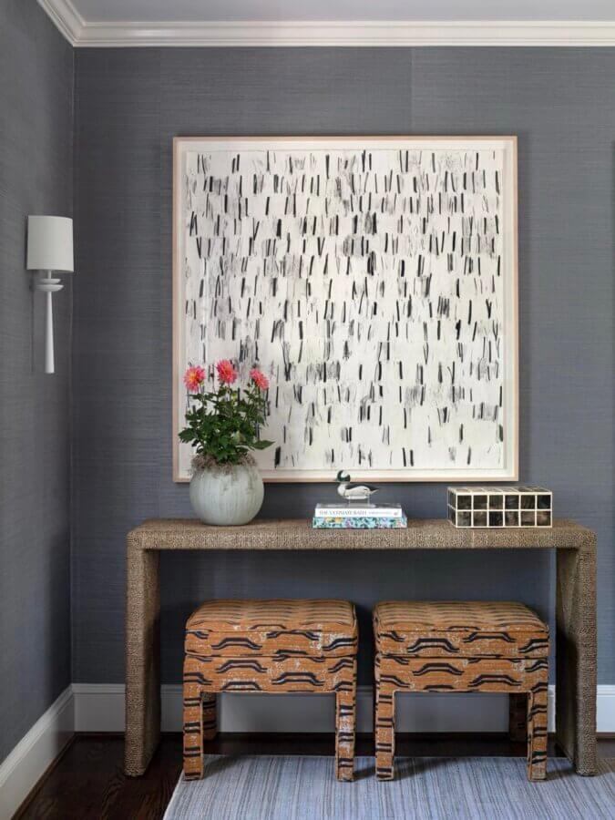 It Started with Wallpaper: Look Inside This Reimagined Richmond Colonial - 8 A console table holds a potted plant, books, and decorative items beneath abstract artwork, with two patterned stools underneath, against a gray wall—showcasing sophisticated interior design inspired by a colorful Richmond home.