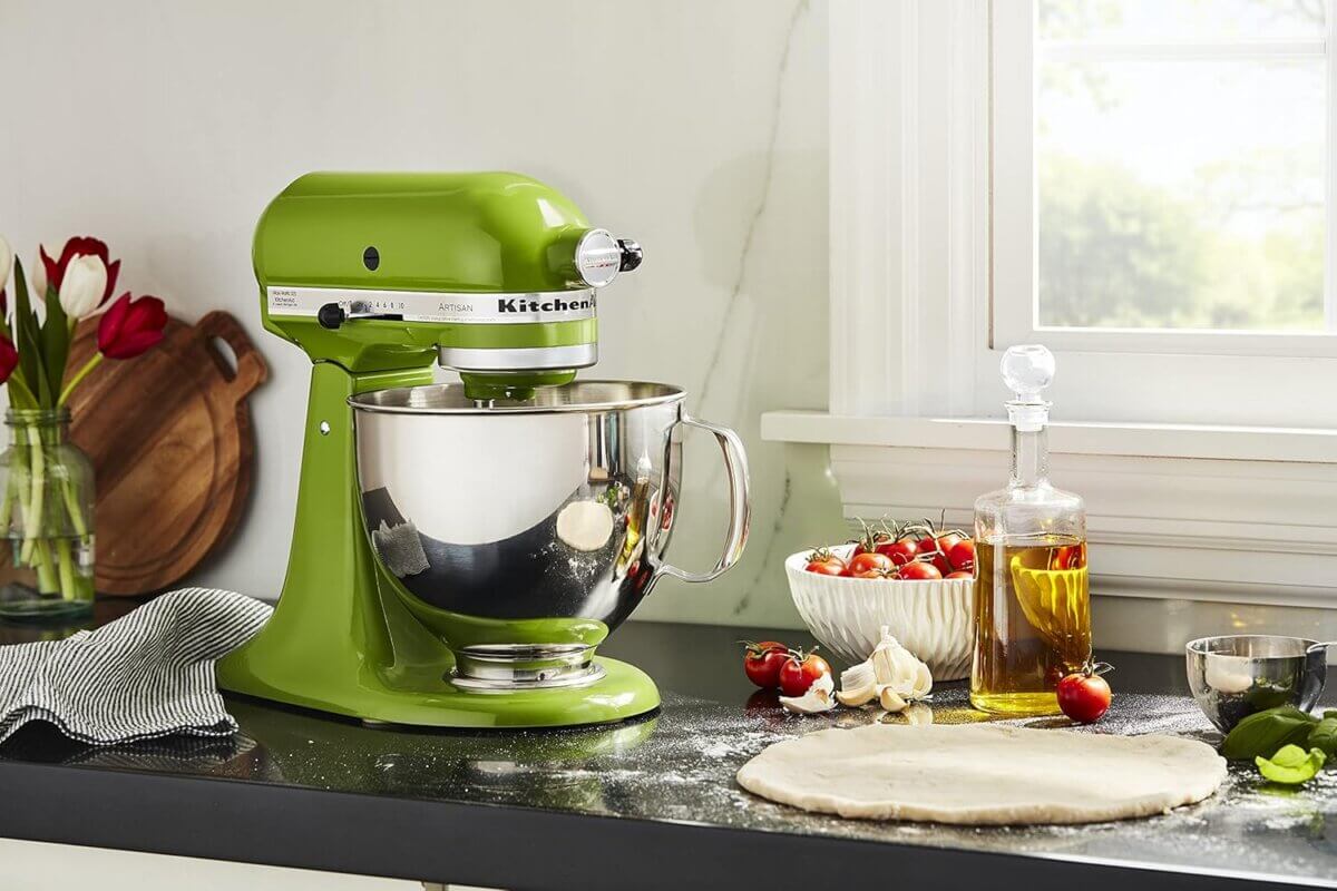 Chefs' Kitchen Tools Worth the Splurge (and Some to Save On) - 3 A green stand mixer, one of the essential chef tools, sits on a kitchen counter beside a bowl of tomatoes, olive oil, and rolled-out dough, with sunlight streaming through a nearby window.