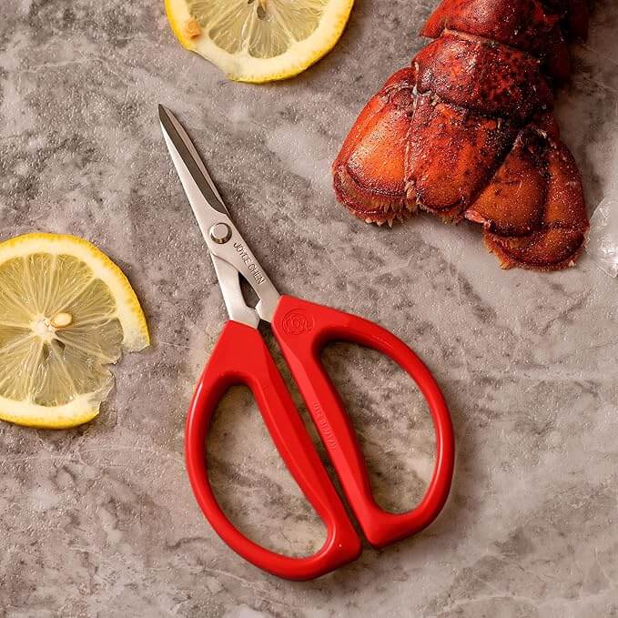 Chefs' Kitchen Tools Worth the Splurge (and Some to Save On) - 11 Red-handled kitchen shears, an essential addition to your chef tools, rest on a gray surface beside two lemon slices and a lobster tail.