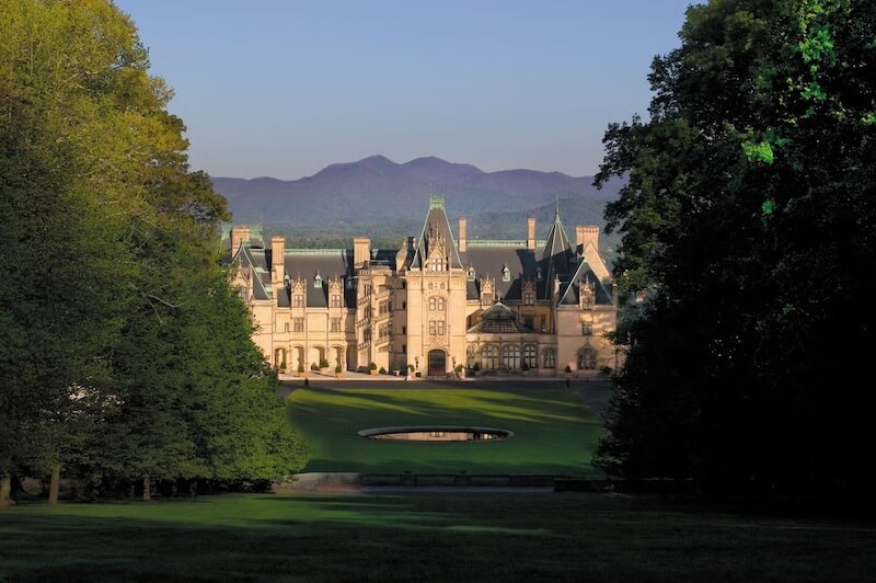 Spend a Weekend 'Wine-Hopping' in Asheville, NC - 6 A large, ornate mansion with multiple gables and chimneys stands on a manicured lawn, surrounded by trees and mountains.