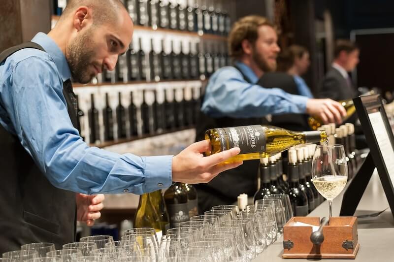 Spend a Weekend 'Wine-Hopping' in Asheville, NC - 8 A bartender pours white wine into a glass at a wine-tasting event in Asheville NC, with wine bottles and glasses arranged on the counter—perfect for a weekend getaway or winery hopping adventure.