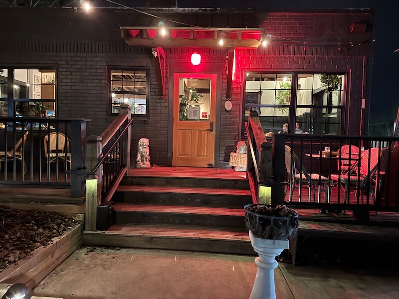 Spend a Weekend 'Wine-Hopping' in Asheville, NC - 10 Wooden steps lead to a restaurant entrance with a red light above the door, outdoor seating on the right, and potted plants by the door—perfect for a weekend night in Asheville NC after a day of winery hopping.