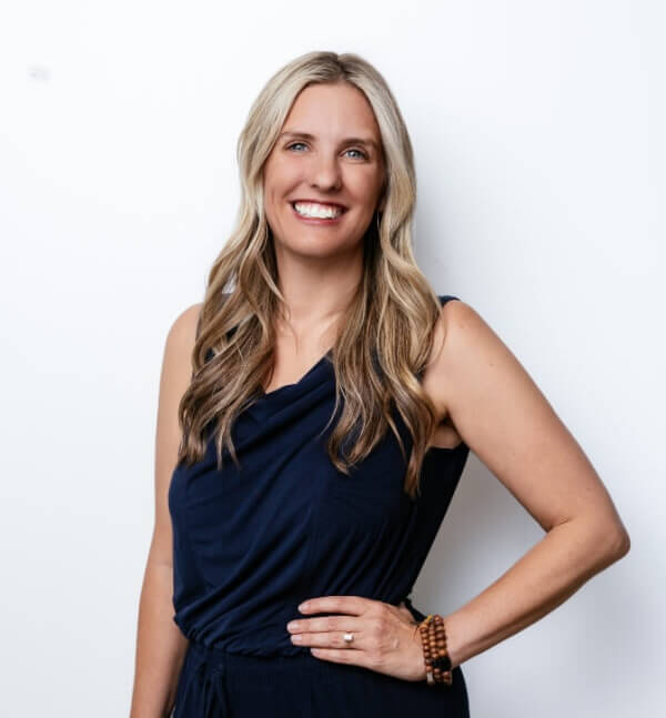Woman with long blonde hair wearing a navy sleeveless dress, standing against a plain white background and smiling at the camera, ready to share financial tips for managing money in my 30s.