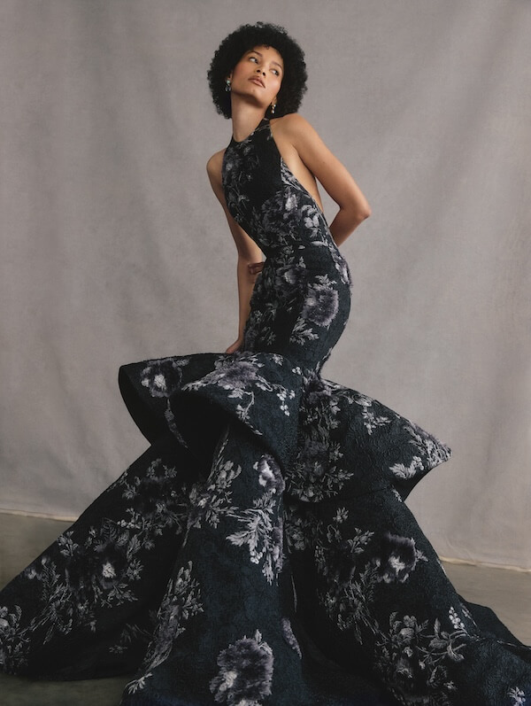 Behind the Nashville Symphony Fashion Show with Marci Houff - 5 A person poses in a dramatic, dark floral mermaid gown with a high neckline and voluminous flared skirt against a neutral backdrop.